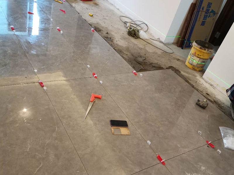 客廳地磚鋪貼：地磚鋪貼前，應(yīng)將地面清掃干凈，尤其是凝結(jié)后的混凝土，否則，地磚鋪貼后會(huì)出現(xiàn)翹邊、空鼓等現(xiàn)象，然后再灑水潤濕地面。地面充分濕潤，但不能有積水，然后將3:1混合好的沙子水泥鋪在地面上，進(jìn)行基層處理。在地磚背面均勻抹水泥砂漿作為粘合層，厚度不低于1cm，然后鋪在剛才試鋪的位置上，用橡皮錘輕敲地磚飾面直至密實(shí)平整達(dá)到要求。地磚鋪完后24h進(jìn)行清理勾縫，勾縫前應(yīng)先將地磚縫隙內(nèi)雜質(zhì)擦凈，用專用填縫劑勾縫，完工后（一般宜在24h之后）再用棉紗等物對(duì)地磚表面進(jìn)行清理。