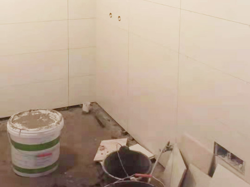 衛(wèi)生間墻面貼磚：首先應除去基層表面的污垢，油漬，浮灰;除去基層上所有涂料層，膩子層;如果基層未能達到平整度要求，需對基層進行預先的找平處理。鋪貼瓷磚前需事先找好垂直線，以此為基準鋪貼的瓷磚高低均勻、垂直美觀;此外，施工前在墻體四周需彈出標高控制線，在地面彈出十字線，以控制地磚分隔尺寸。對瓷磚的色彩、紋理、表面平整等進行嚴格的挑選，然后按照圖紙要求預鋪。對可能出現(xiàn)的尺寸、色彩、紋理誤差等進行調(diào)整、交換，直至達到最佳效果。 調(diào)制粘結劑：加水后將粘結劑漿料攪拌至潤滑均勻，無明顯塊狀或糊狀結塊，攪拌后的漿料靜置5-10分鐘后再稍加攪拌1-2分鐘即可使用。 將瓷磚平整地鋪貼在基層上，使用橡膠錘將瓷磚拍實鋪平。施工過程中，可小幅度轉動瓷磚，使?jié){料與瓷磚背面充分接觸。